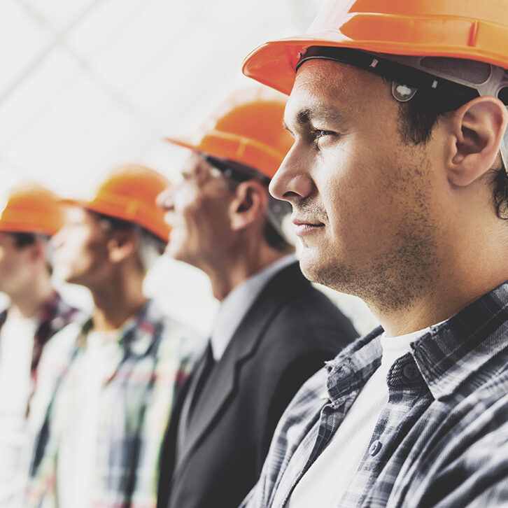 Close up. Standing Industrial Engineers in Shirts and Orange Helmets. Modern Construction and Engineering Concepts. Safety of Work in Production and Construction. Hard Work on Project.